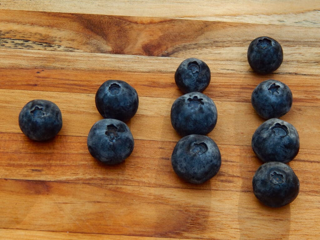 10 blueberries sorted into number groups on a wooden board by a preschooler