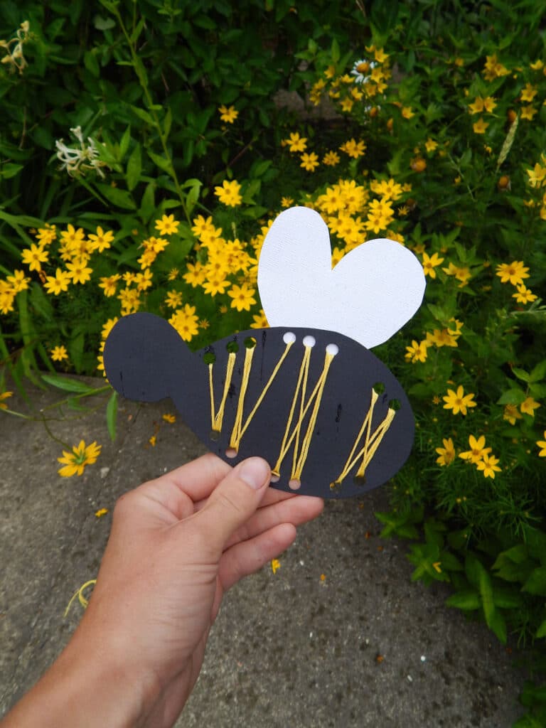 hand holding a DIY handmade bee craft for kids outside in the garden yellow flowers in background