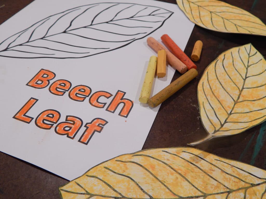 beach leaf coloring page with yellow, orange, and tan oil pastels, with three colored and cut out leaves on a table 