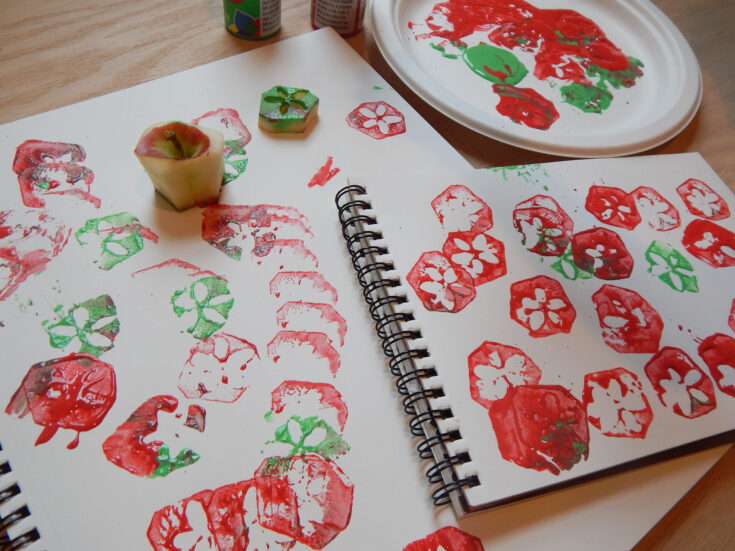 process art made with apple cores on spiral bound blank notebooks with red and green acrylic paint on a paper plate with two apple cores on the paper