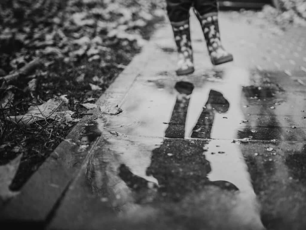 child in rain boots walking in a puddle in black and white