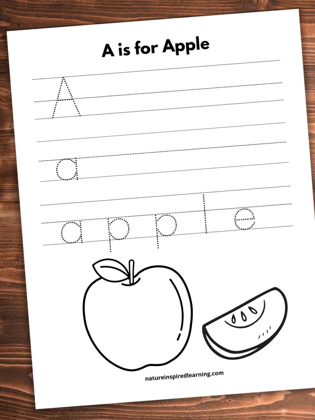A is for Apple written in bold across top with lines with the letter A and a and a third set of lines with apple written in lowercase dotted letters. Black and white image of an apple with one slice across bottom half of worksheet. Printable slanted on a wooden background.