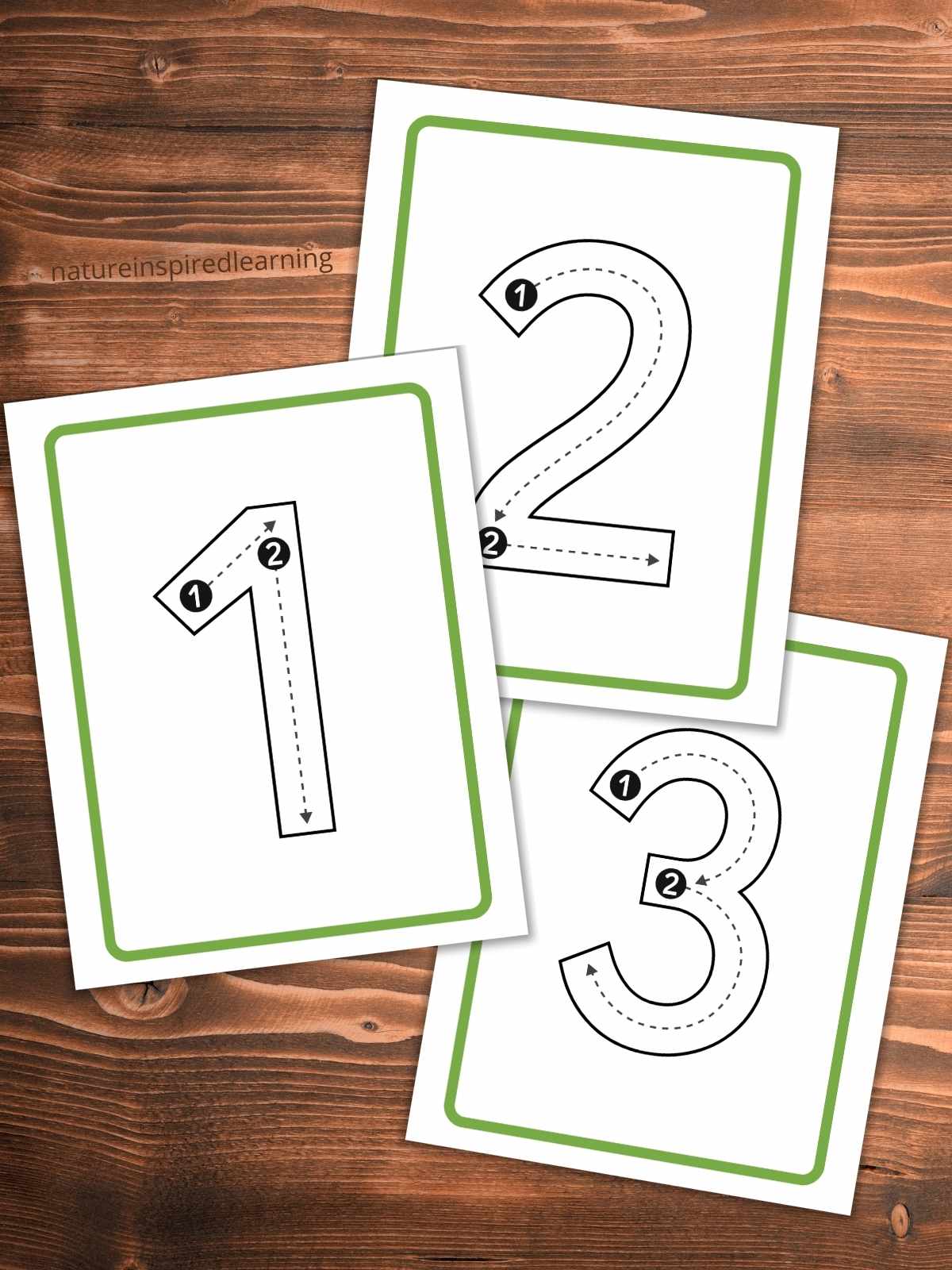 cut out number cards with numbers 1, 2, and 3 in outline form with tracing lines and numbers. Cards overlapping each other on a wooden backgound