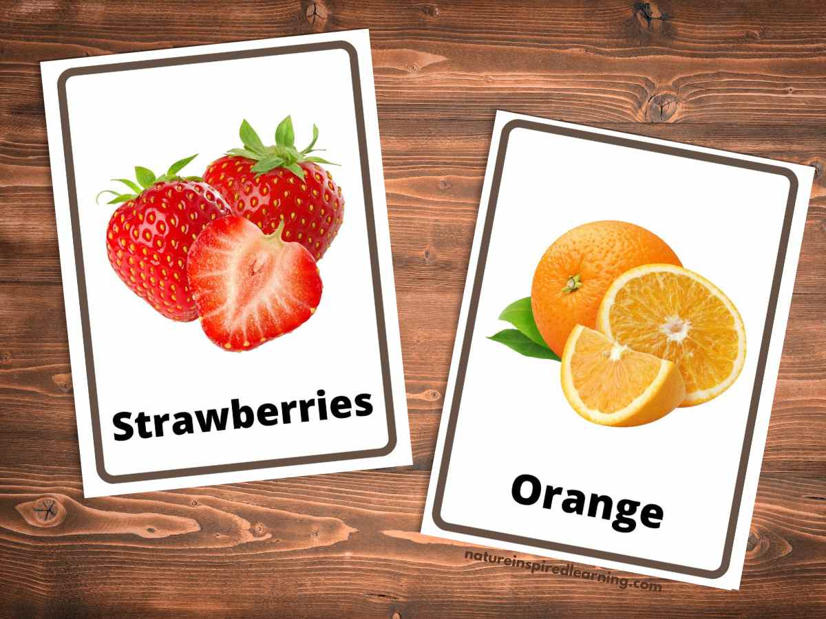 A strawberry flashcard with the word and real life strawberries next to an orange flashcard with cut oranges as the picture. Wooden background behind the cards.