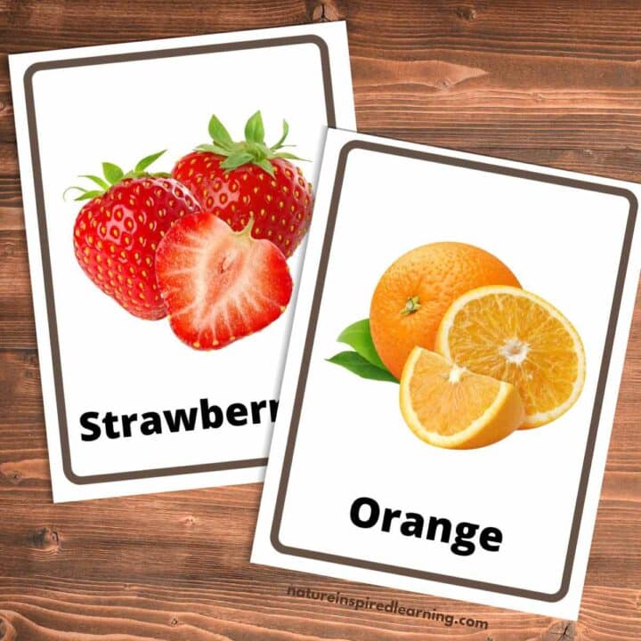 A strawberry flashcard with the word and real life strawberries next to an orange flashcard with cut oranges as the picture. Wooden background behind the cards.
