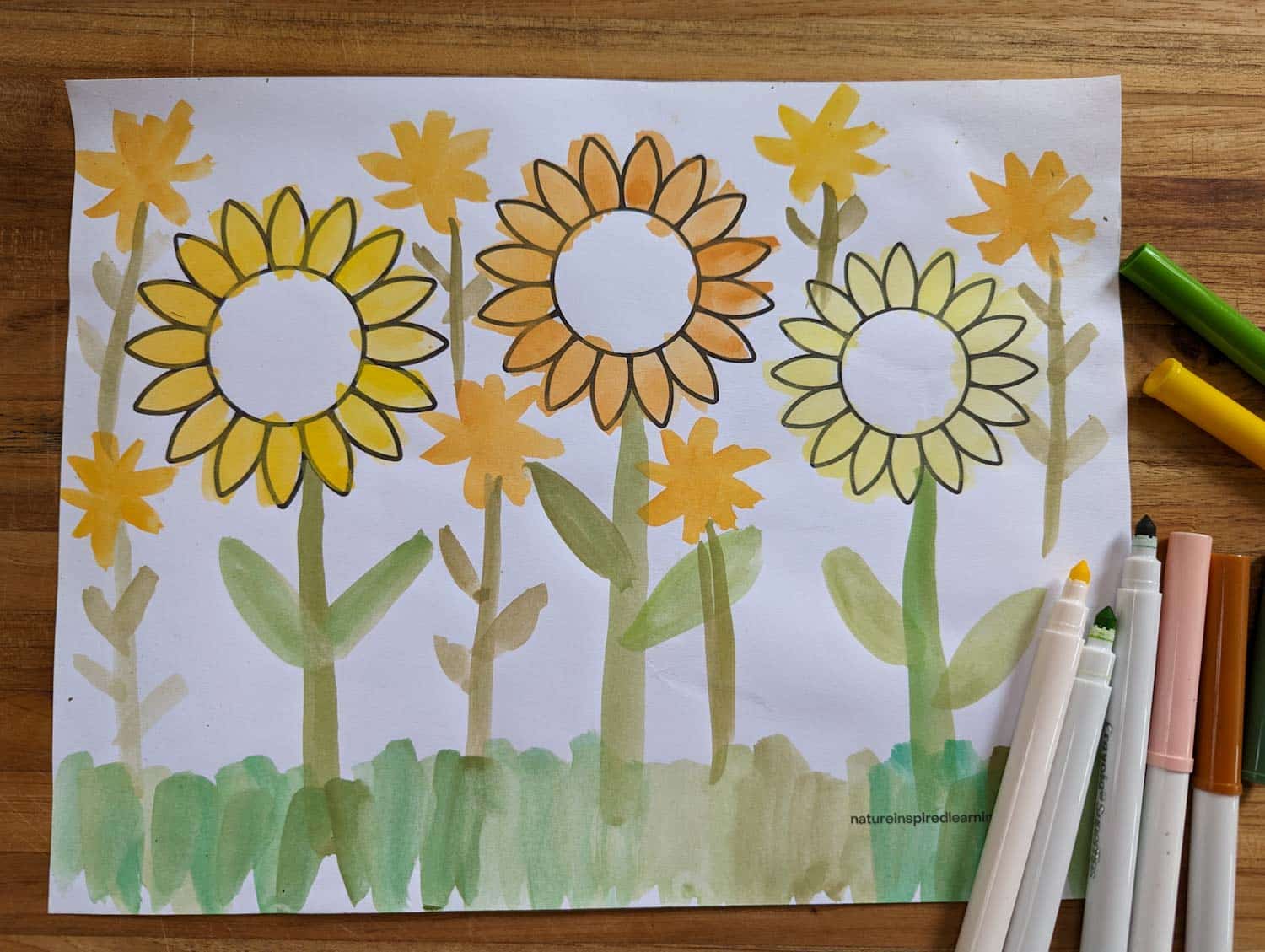 printed off sunflower coloring page on a wooden board with markers on the bottom right with some covers removed
